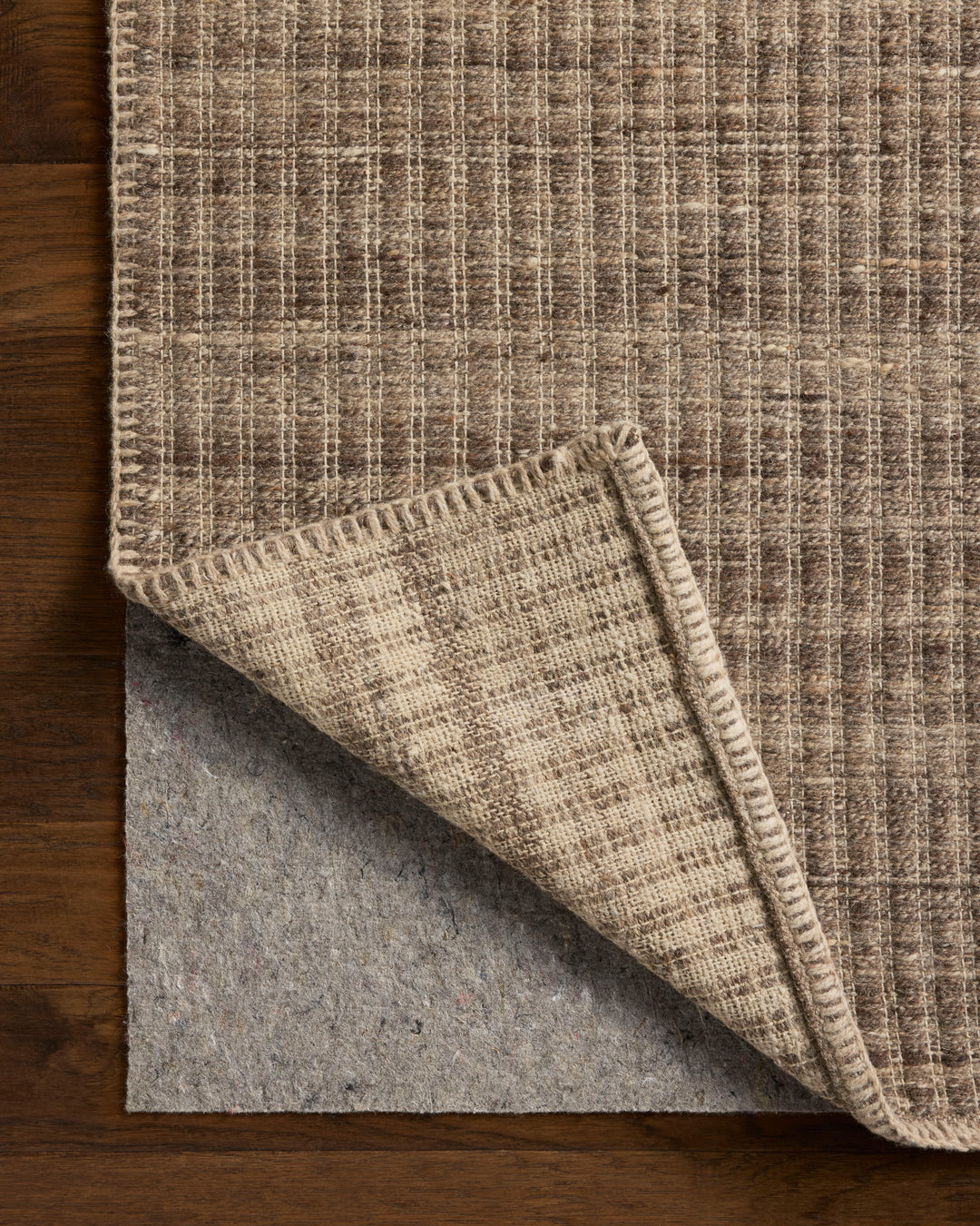 Elm Bark colour textured rug with a folded corner on a wooden floor. Felt rug pad showing underneath 