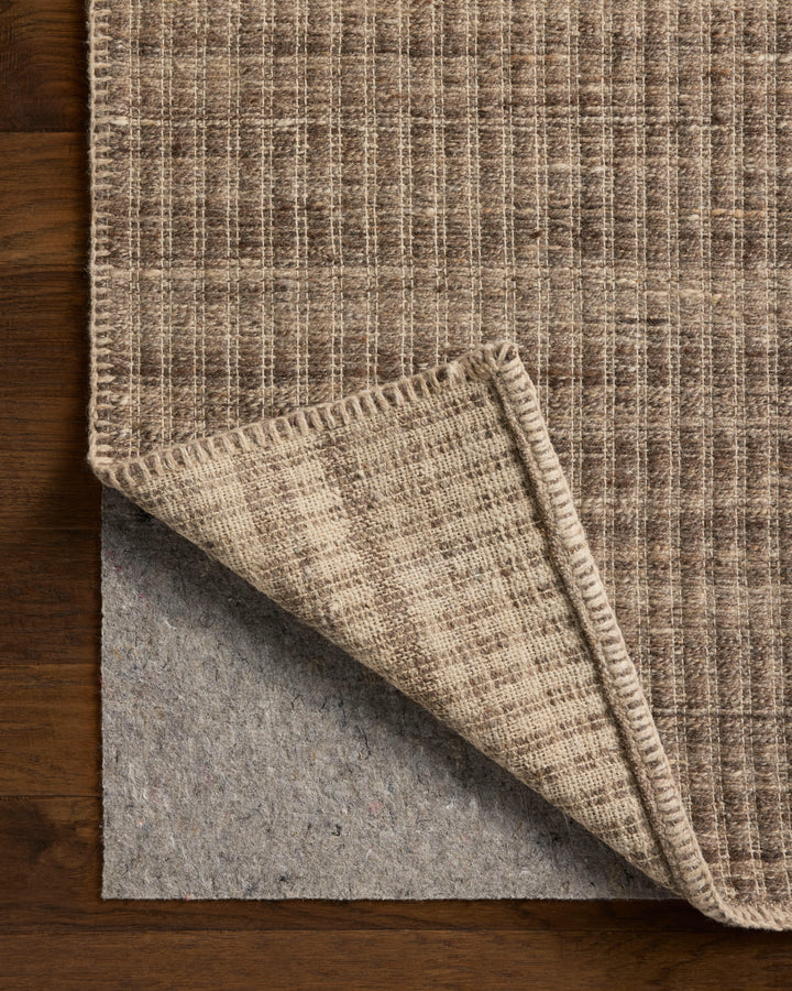 Elm Bark colour textured rug with a folded corner on a wooden floor. Felt rug pad showing underneath 