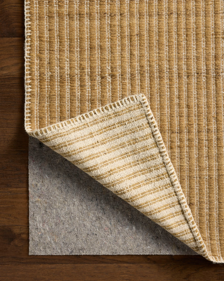 Textured Elm wheat beige rug with a corner folded over showing the backing and felt rug pad on a wooden floor.