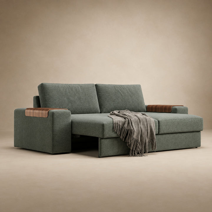 Vilander Sofa Bed with Wide Arms in 281 Boreal Green textured upholstery, featuring walnut wood armrest accents and a modern design, shown against a warm beige studio background.